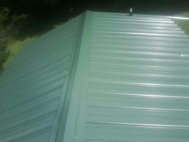 New green metal panels meeting at the ridge of a roof — Flat Roof Repair work by our crew in Hopkinsville