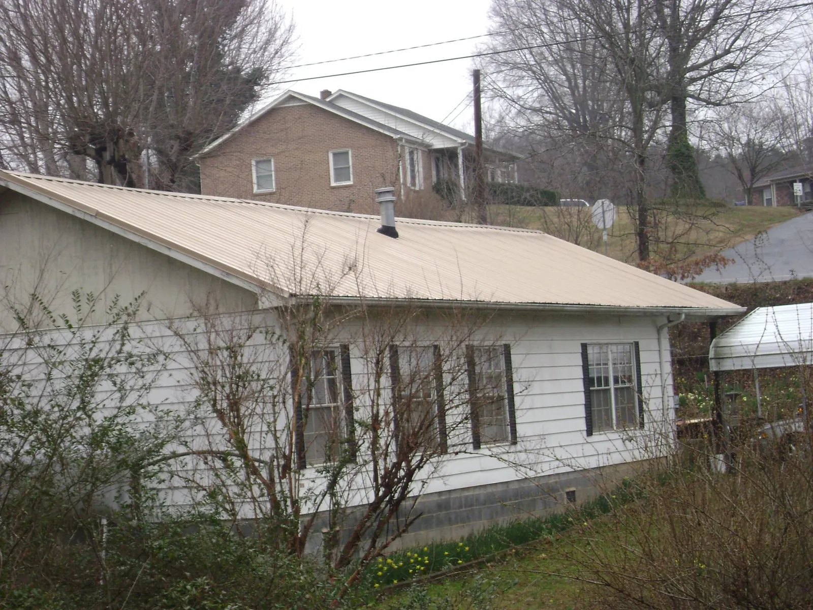 Tan metal roof on a white sided house set into a hillside — Commercial Roofing by Roofing Brothers in Hopkinsville